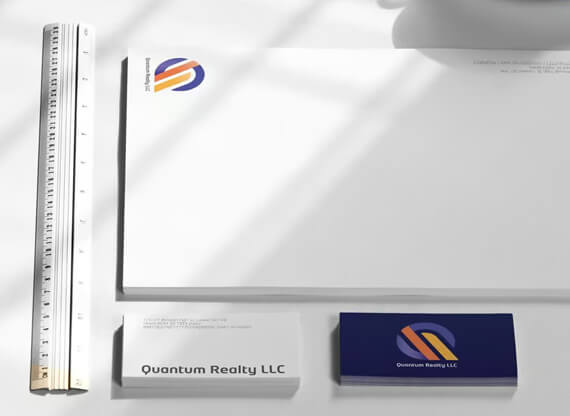 Geschäftsausstattung von „Quantum Realty“ auf weissem Schreibtisch, bestehend aus Visitenkarten, Briefbogen, Lineal und einem interessanten Schattenwurf.