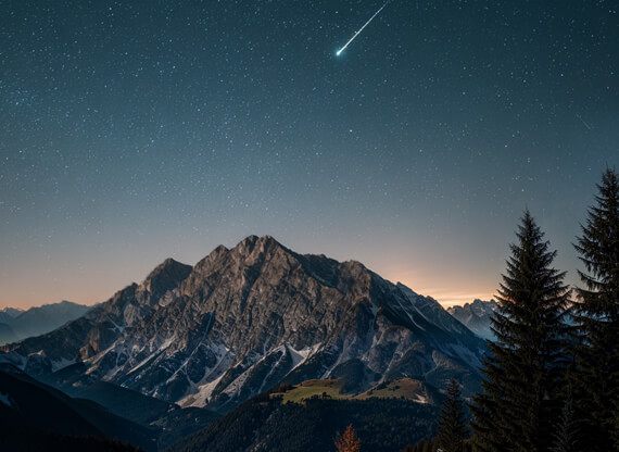 Positionierungsstrategie-570x416px Die Erarbeitung einer Positionierungsstrategie wird durch eine nächtliche Sternenlandschaft über einem bayerischen Berggipfel dargestellt, wobei eine leuchtende Sternschnuppe die zukunftsweisende Ausrichtung symbolisiert.
